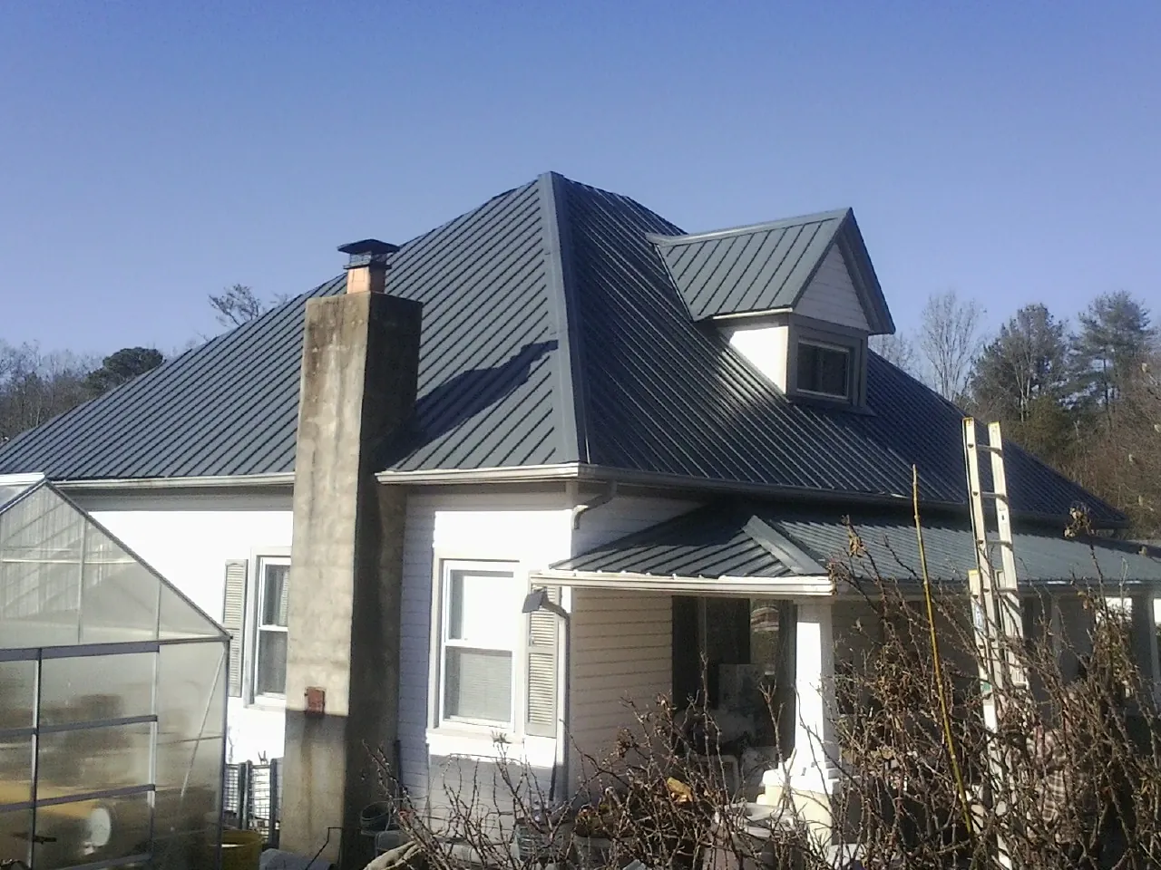 Dark blue standing seam metal roof on a white farmhouse with dormer — Slate & Tile Roof Repair by Roofing Brothers in Charles Town