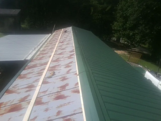 Old rusted panels beside newly installed green metal roofing — Wind Damage Roof Repair by Roofing Brothers in Charles Town