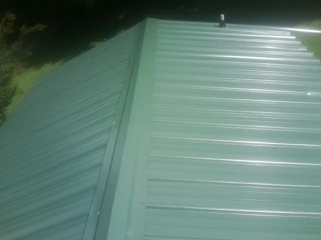 New green metal panels meeting at the ridge of a roof — Flat Roof Repair work by our crew in Charles Town
