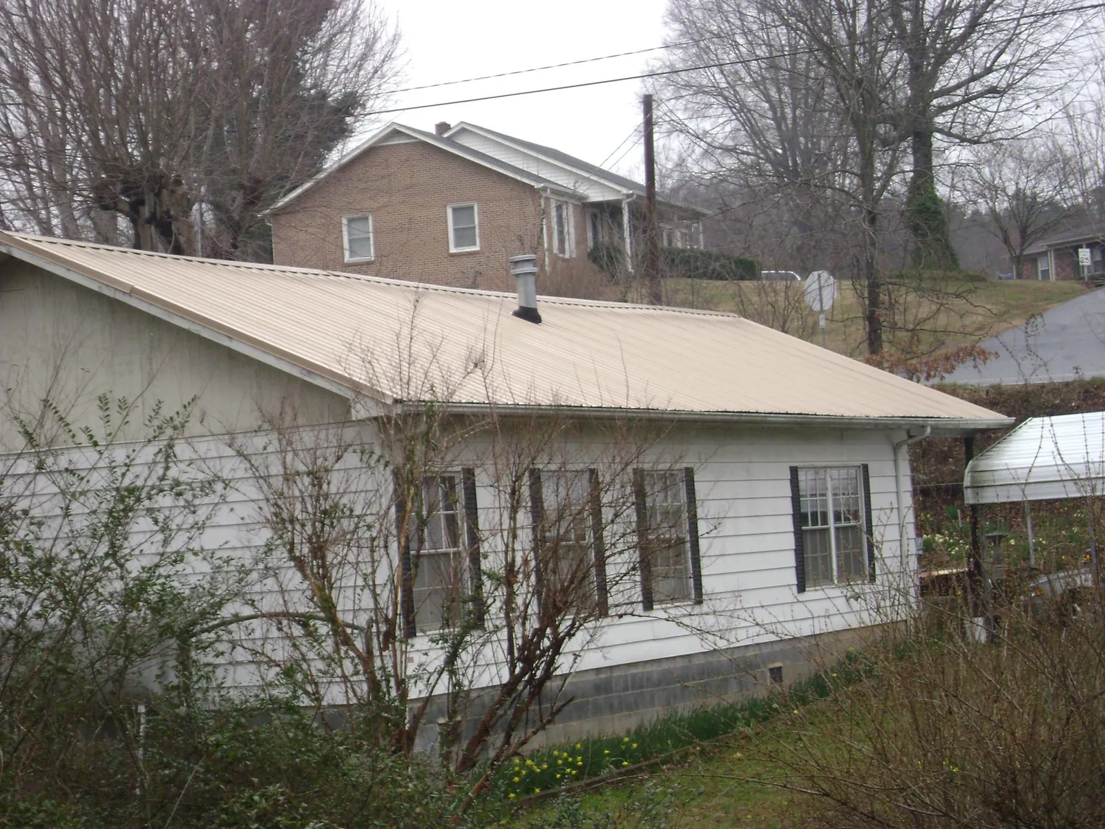 Tan metal roof on a white sided house set into a hillside — Commercial Roofing by Roofing Brothers in Charles Town